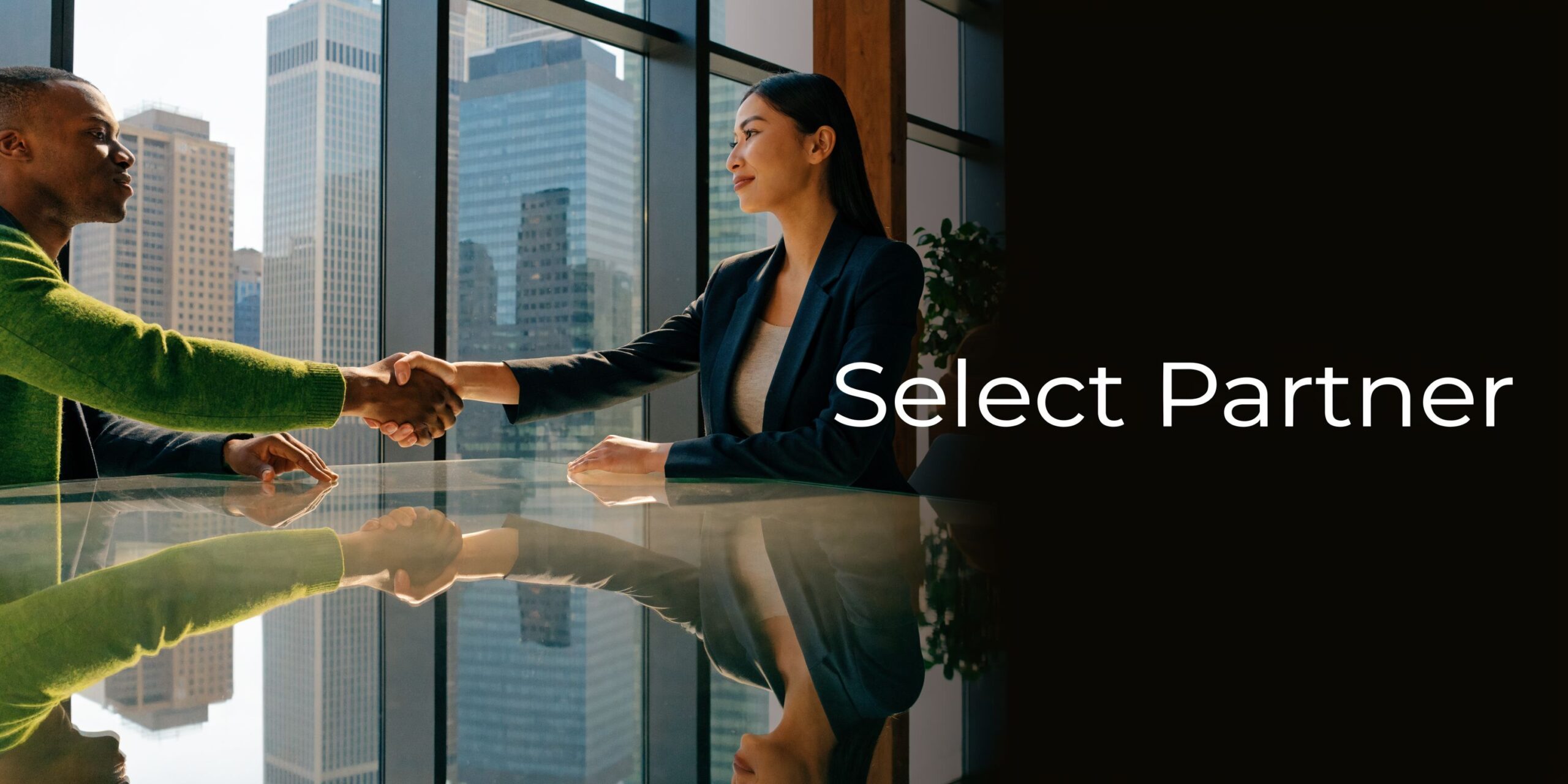 A professional man and woman shaking hands over a glass table in an office with city views.