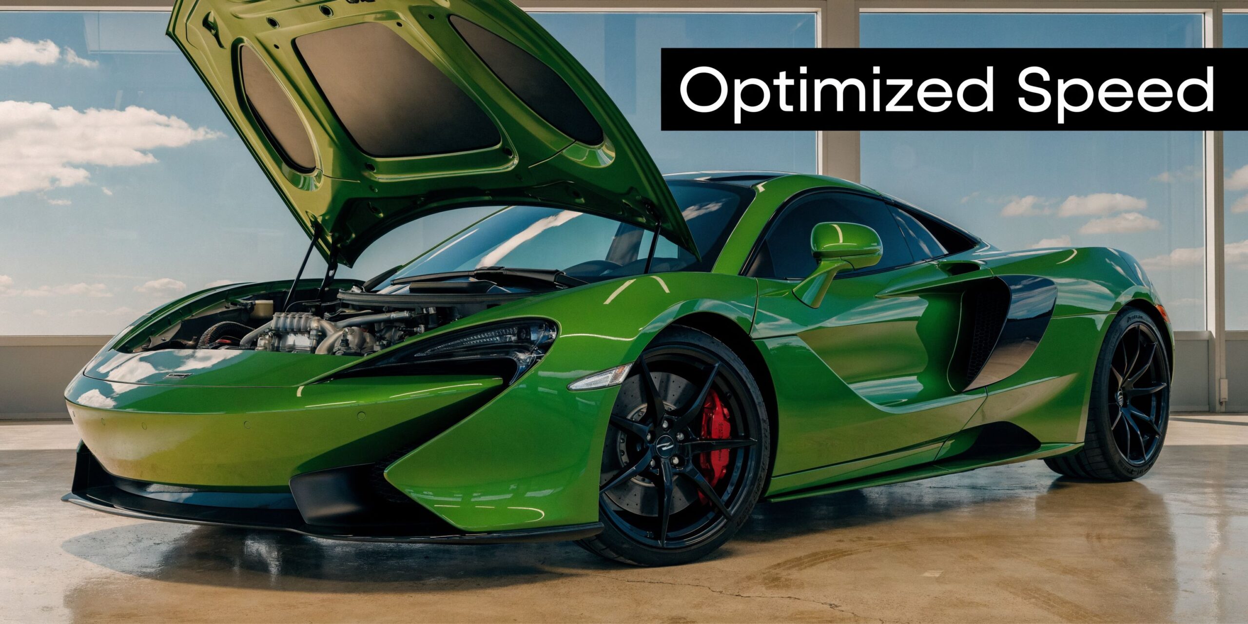 A vibrant green McLaren sports car with an open hood displayed in a modern showroom setting.